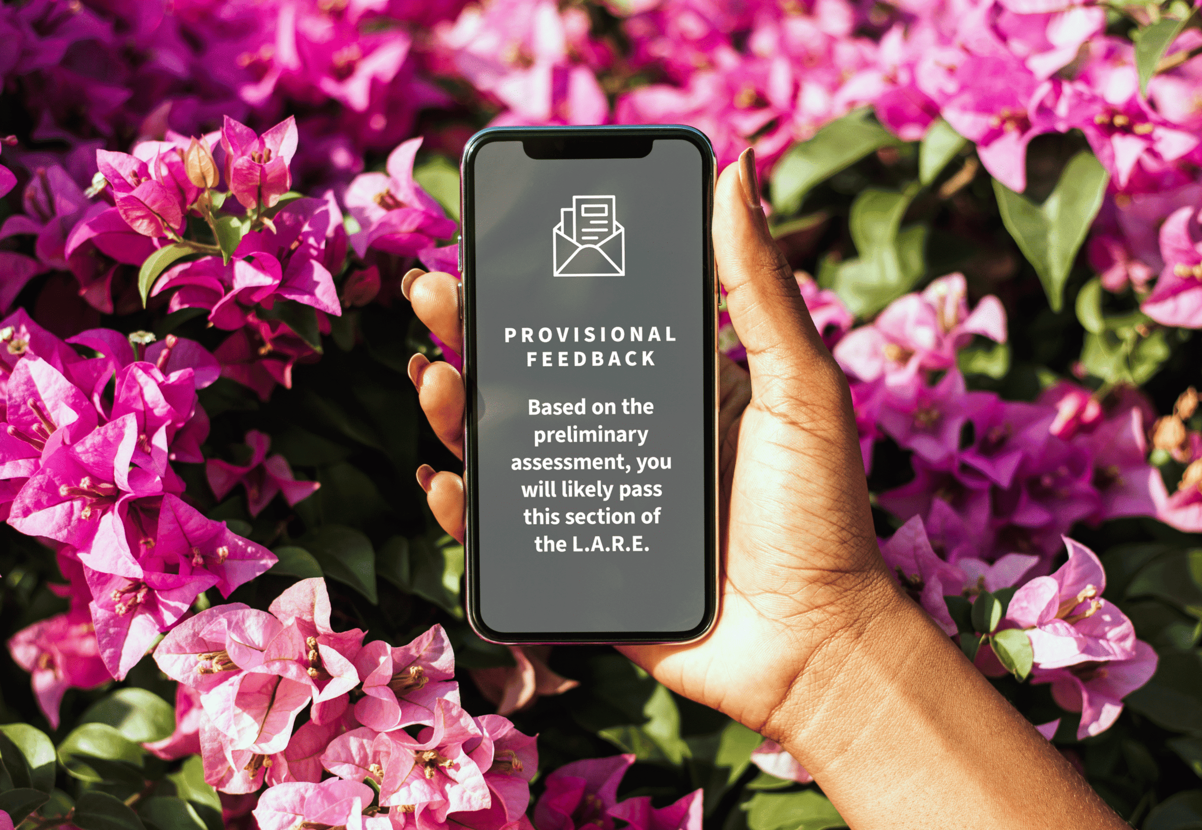 Photo of a hand holding a cell phone in front of pink flowers. On the screen, the email message says Based on the preliminary assessment, you will likely pass this section of the L.A.R.E.