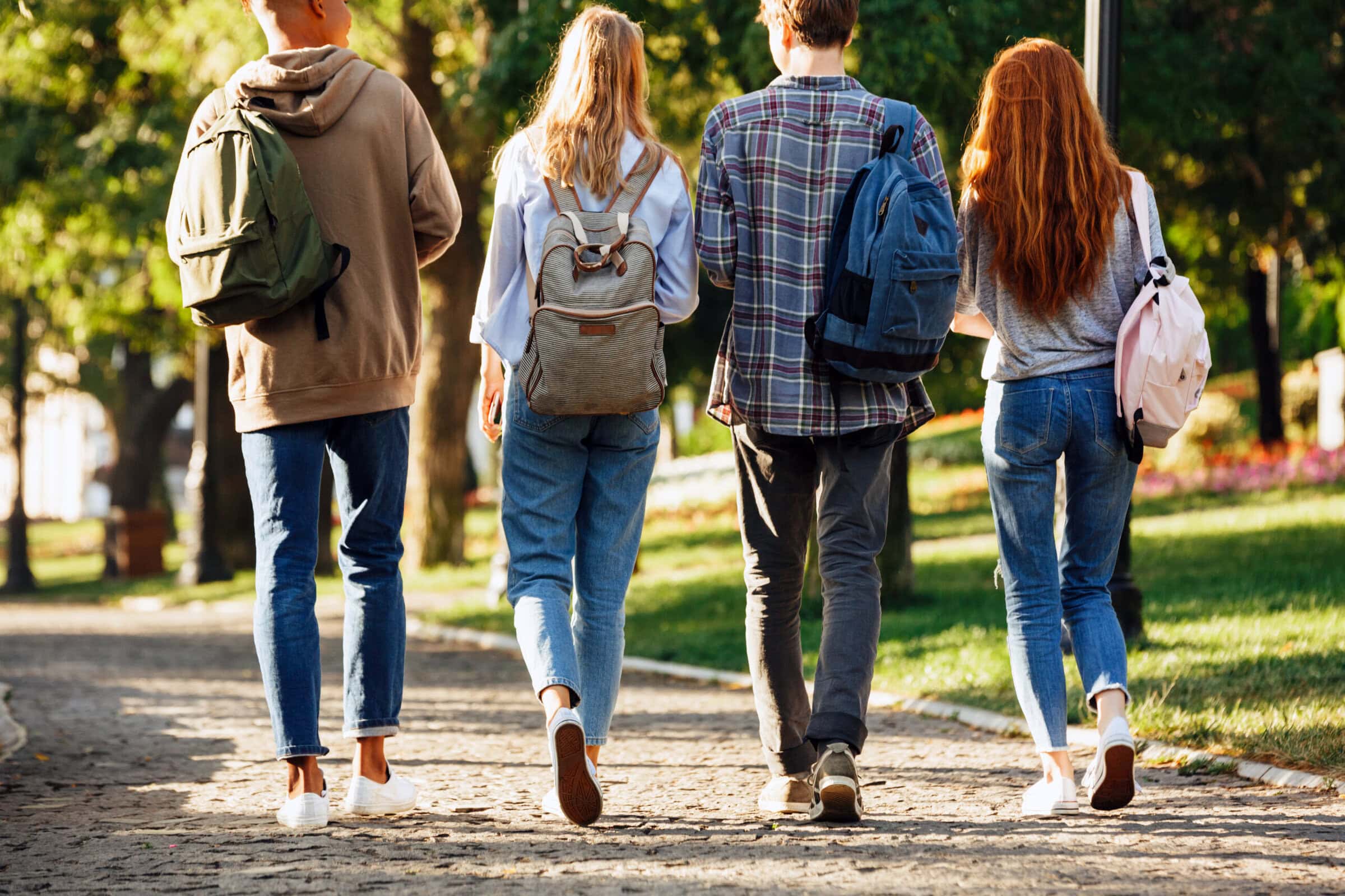Back view group of students with backpacks walking on a college campus outdoors