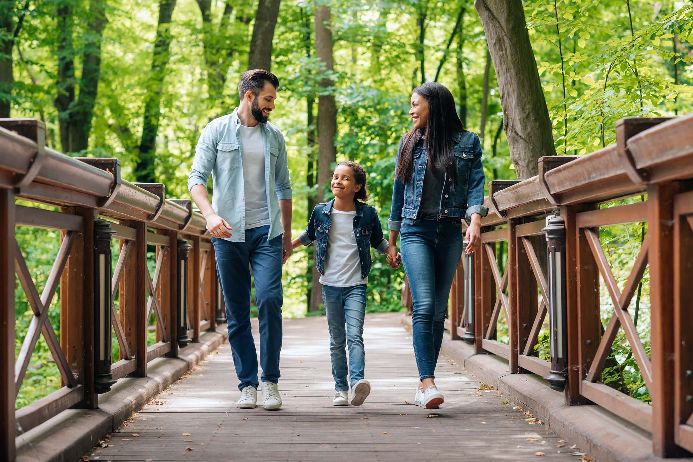 young smiling family holding hands and walking through the wooden bridge in forest