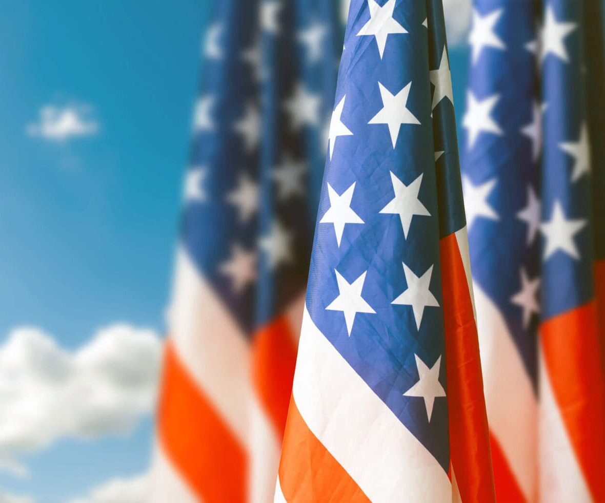 Large flag of usa waving in the wind against the sky with clouds on sunny day