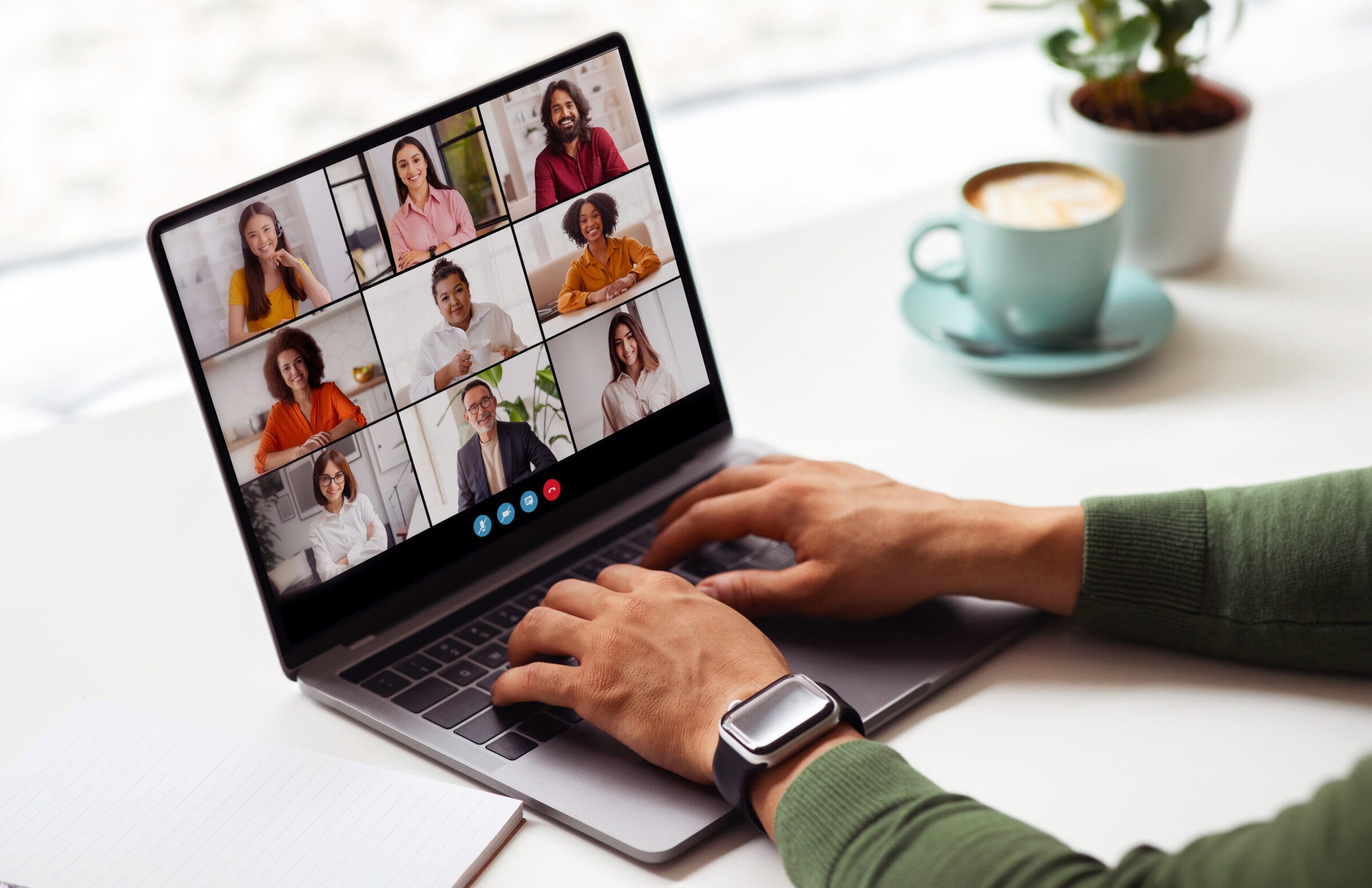 Man working on a laptop, participating in a video conference with several other people. The laptop screen displays a grid of video windows, showing the faces of the participants.