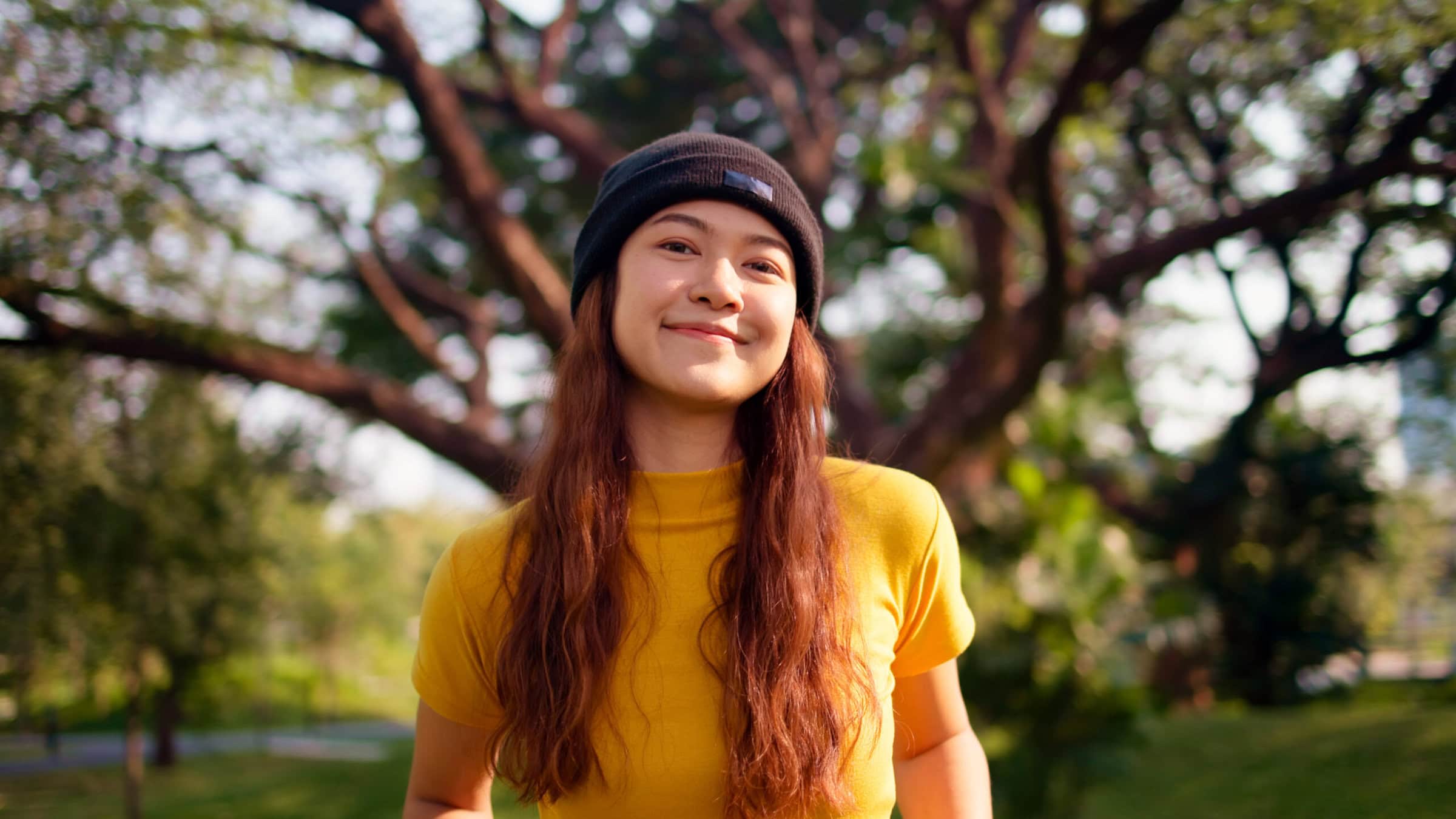 Young person in a park by a tree in sunlight