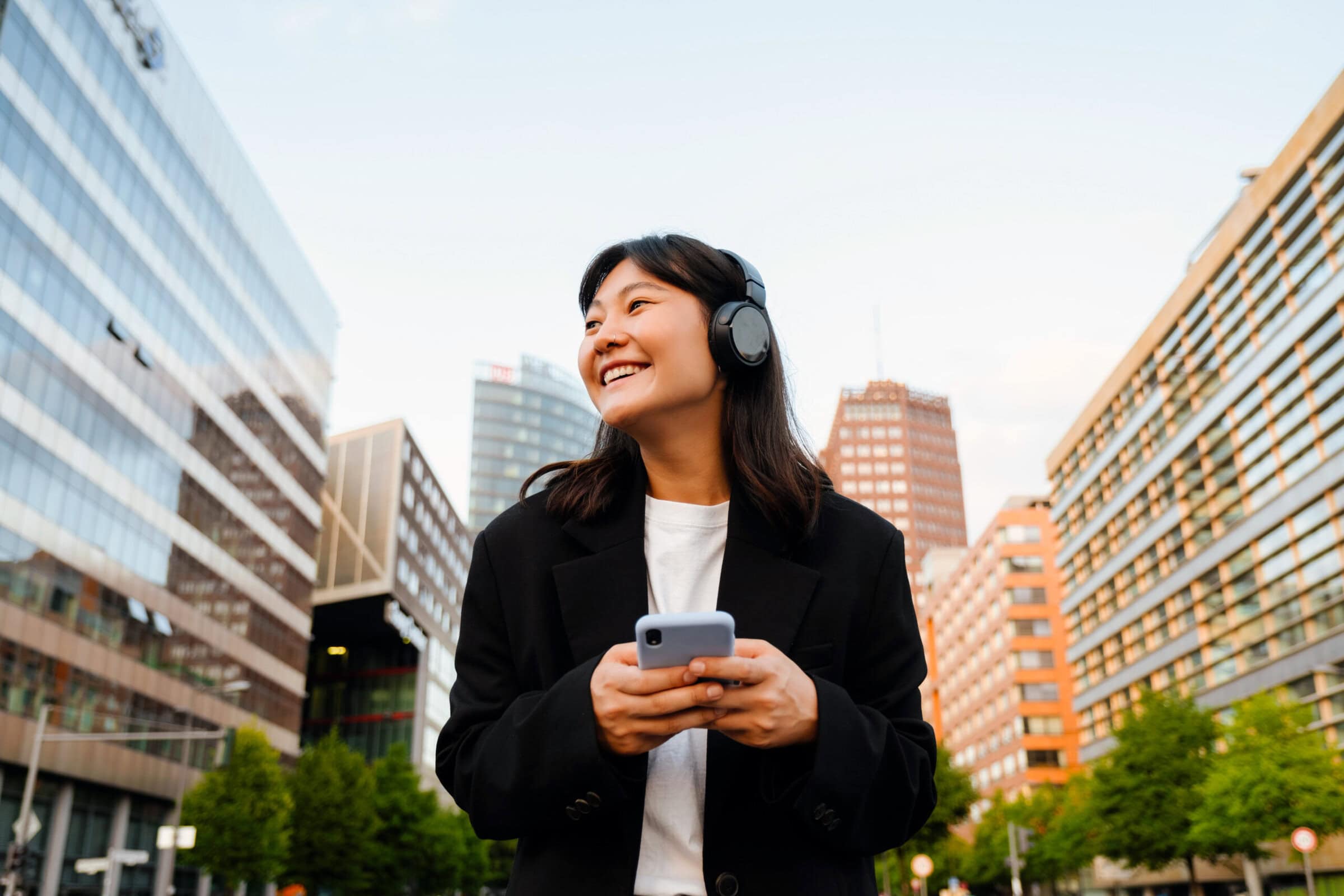Young woman using cellphone and headphones while walking on city street