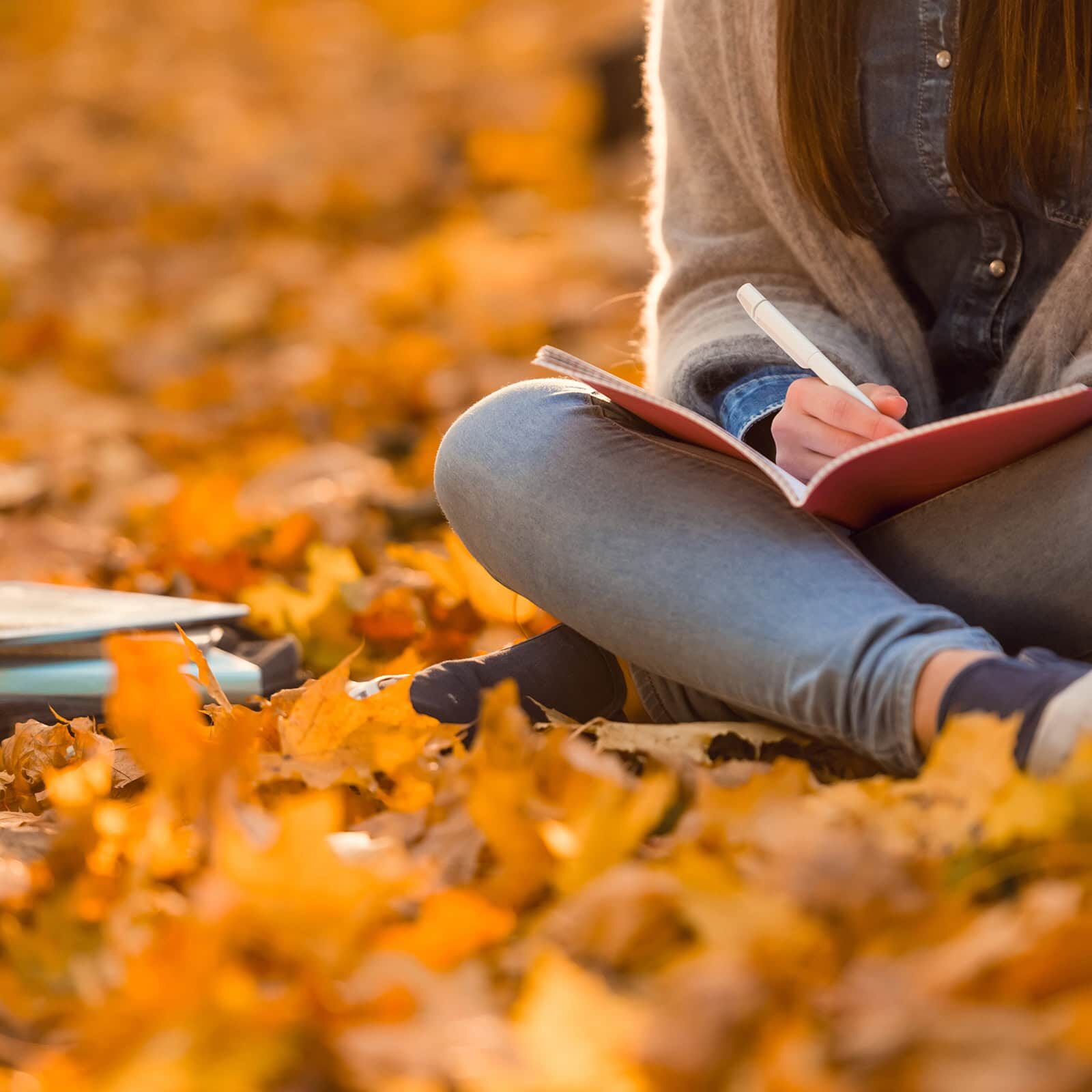 Female student seated in autumn leaves studying